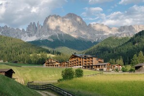 Un albergue de montaña con varias construcciones de madera, rodeado de exuberante vegetación y montañas escarpadas al fondo.