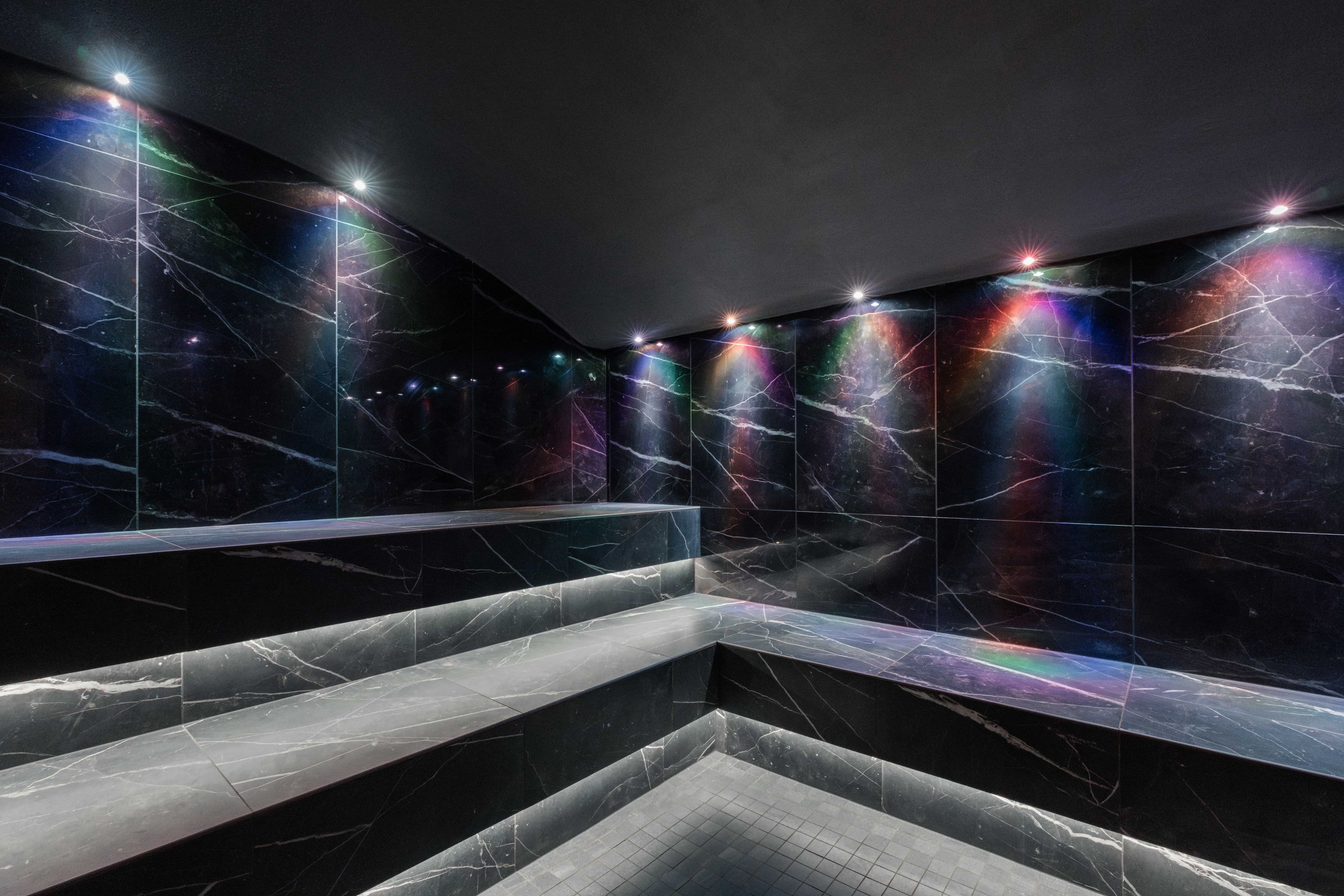 Un baño moderno con paredes de mármol oscuro y una zona de estar central.
