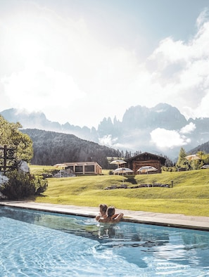 A swimming pool with a view of mountains and a wooden cabin in the background.