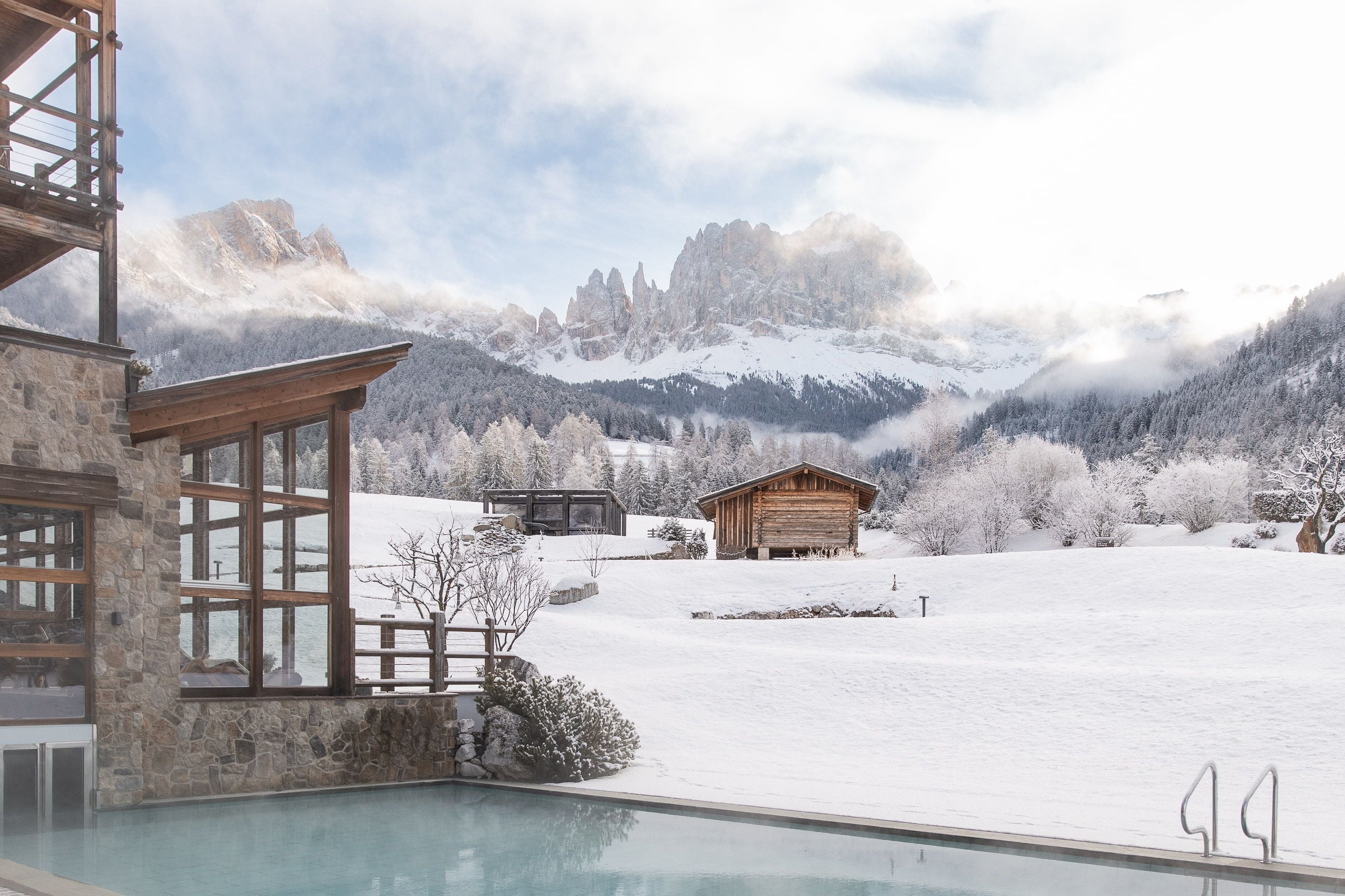 A snow-covered landscape with a wooden cabin and a stone building with large windows.
