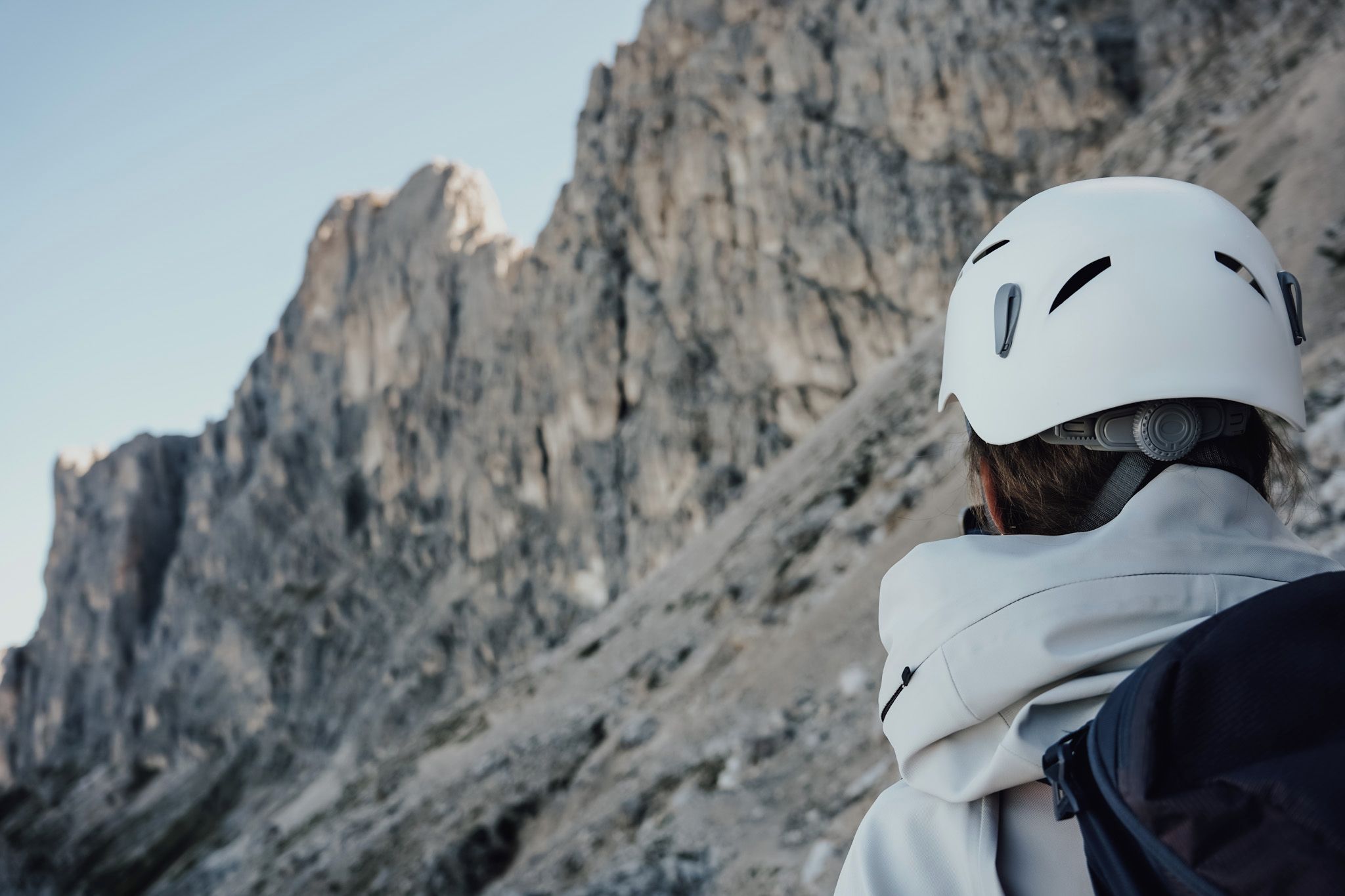 A person wearing a helmet and jacket, facing a rocky mountain.