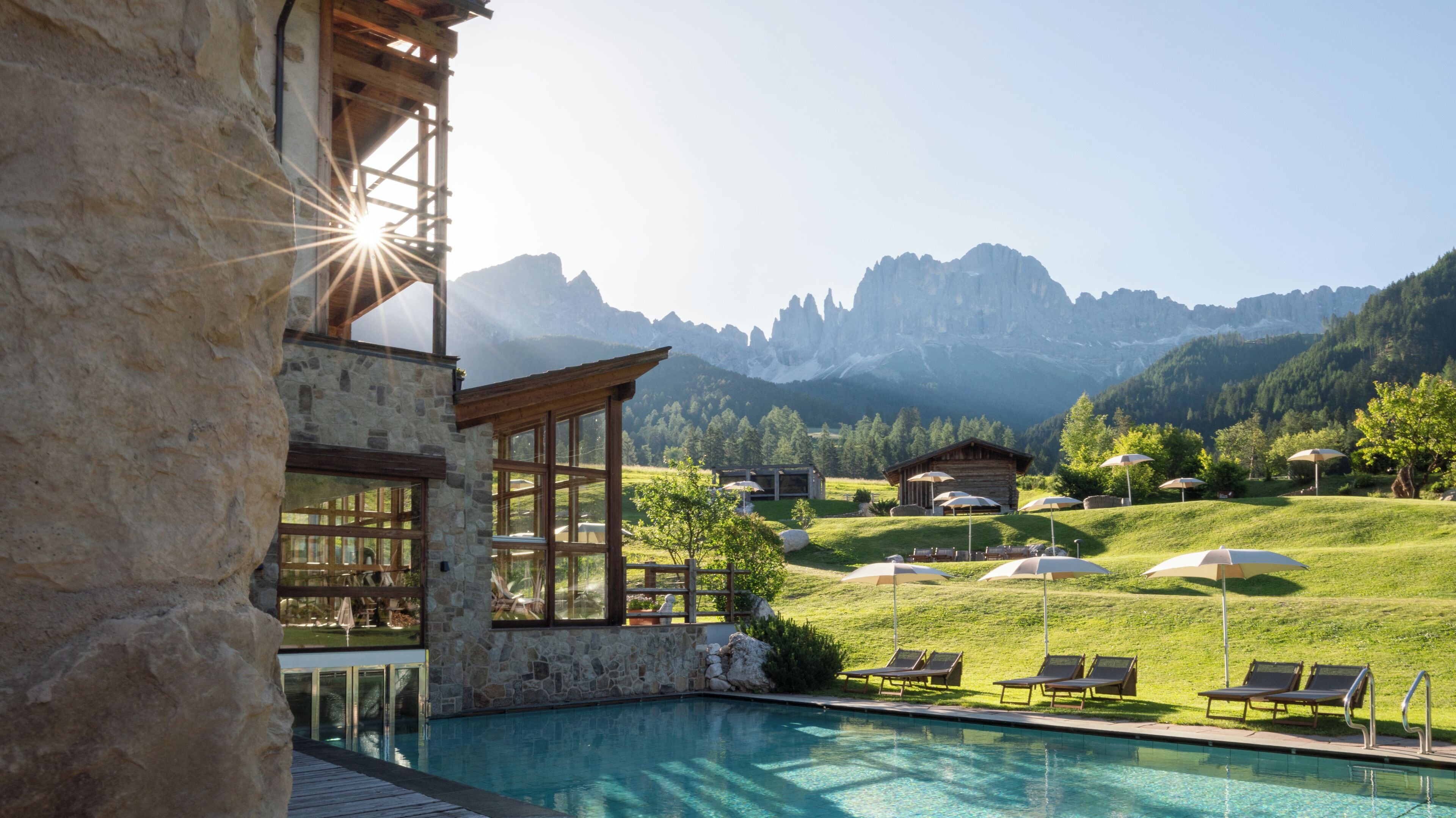 Ein Poolbereich mit Liegestühlen, ein Steinhaus und Blick auf Berge.
