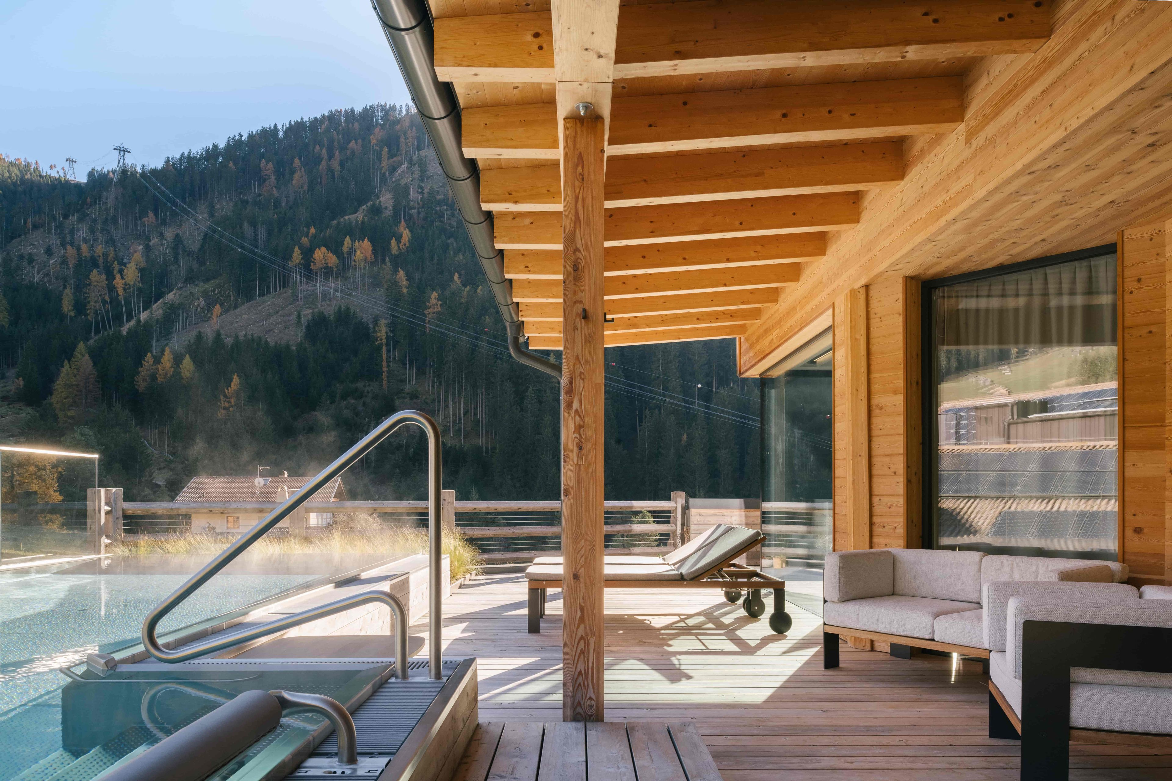 A wooden deck with a pool, lounge chairs, and a sofa.