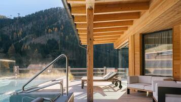 A wooden deck with a pool, lounge chairs, and a sofa.