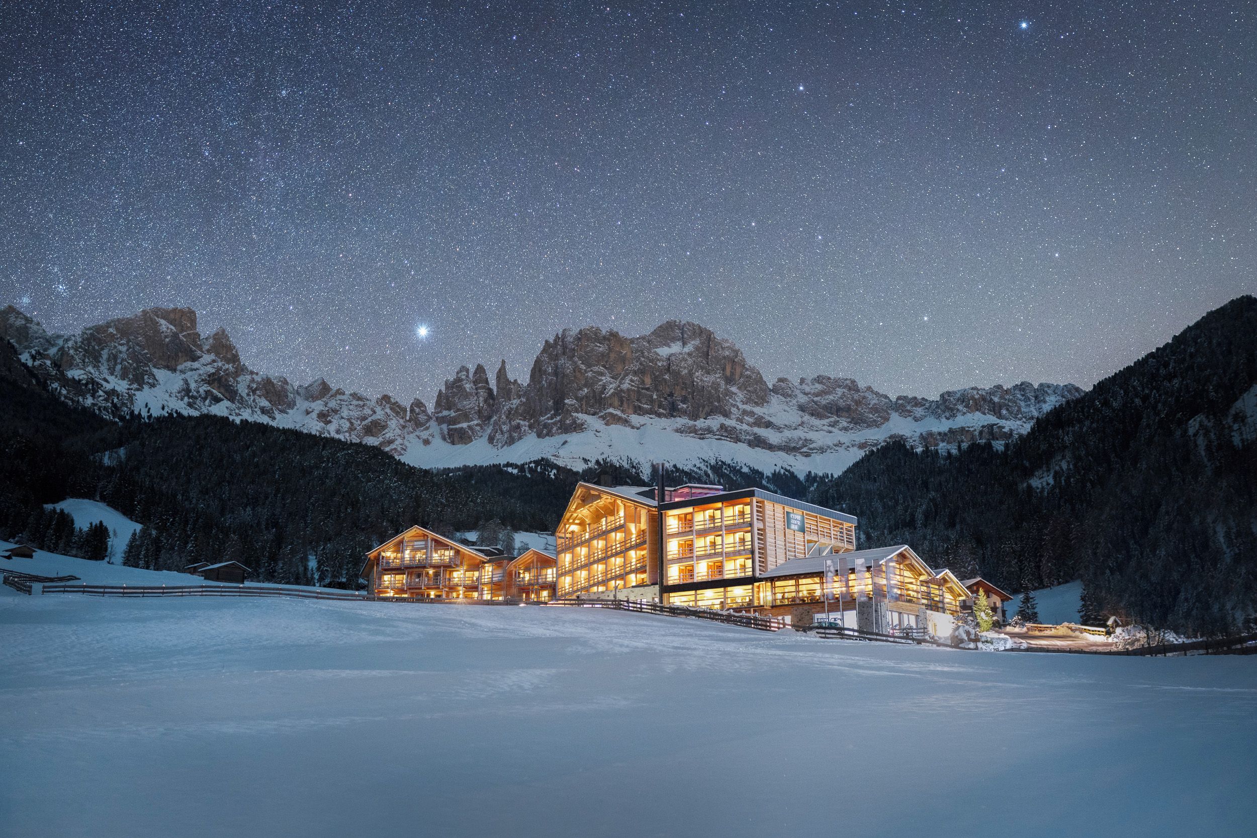 A lodge with multiple wooden buildings, a snow-covered landscape, and a starry night sky.