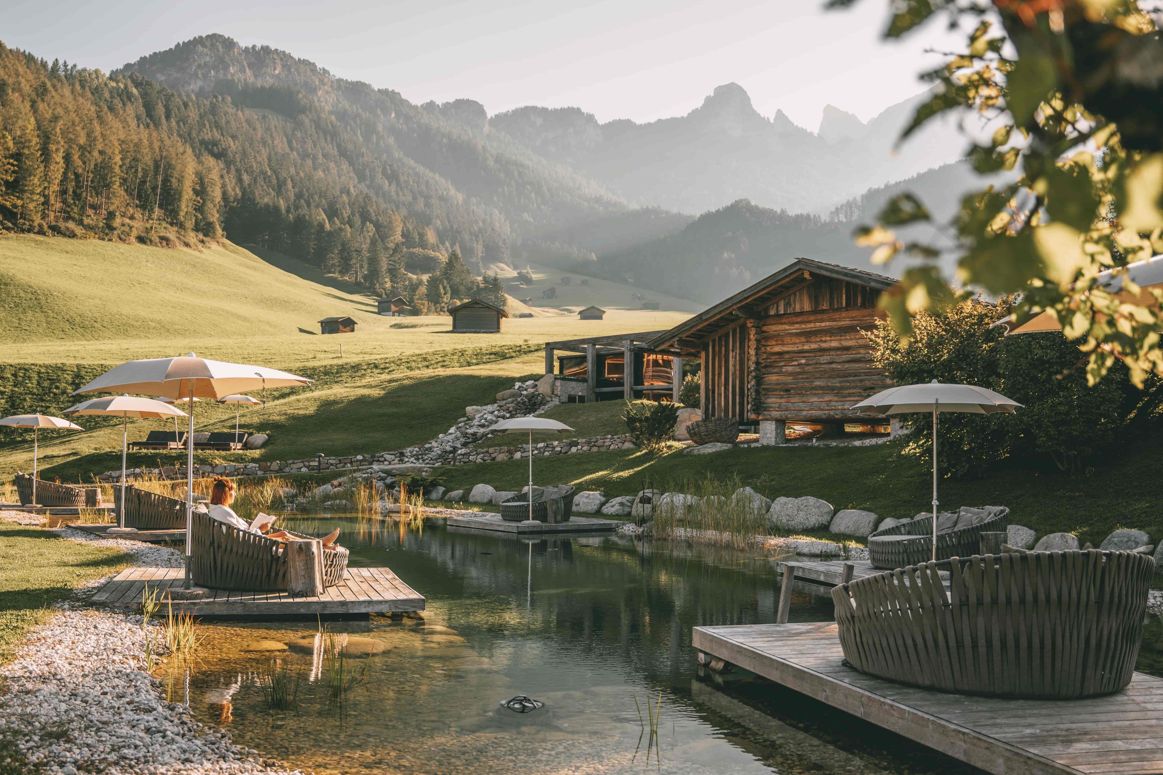 A lakeside resort with wooden cabins, outdoor seating, and a clear view of the surrounding mountains.