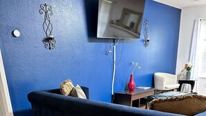A living room with a dark blue sofa, a flat-screen TV mounted on the wall, and a wooden floor.