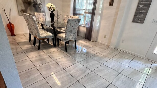 A dining area with a table and four chairs, a vase with flowers, and a painting on the wall.