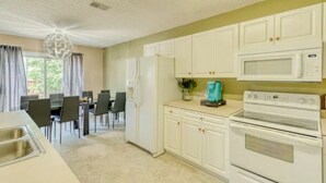 A kitchen with white cabinets, a microwave, and an oven. There is a dining area with chairs and a table visible in the background.