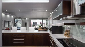 Une cuisine moderne dotée d’un îlot central, d’appareils électroménagers en acier inoxydable et offrant une vue sur le paysage urbain grâce à de grandes fenêtres.