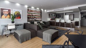Un salon moderne avec un canapé d’angle gris, un coin repas avec une table noire et une cuisine en arrière-plan.