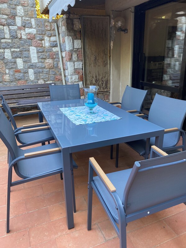 An outdoor patio with a stone wall, a metal grill, and a table with chairs. - Villa Neptune (Palermo)