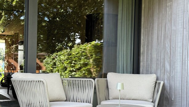 A modern outdoor seating area with two chairs and a round table, set on a tiled floor with a green mat. - The SeeQuartier - A place to arrive, take a deep breath and enjoy Lake Starnberg (Seeshaupt)