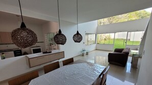 Une cuisine moderne avec des meubles blancs, une table à manger recouverte d’une nappe blanche et des suspensions en osier.