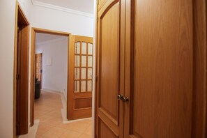 A hallway with wooden doors, a tiled floor, and a view into a room with a lamp.