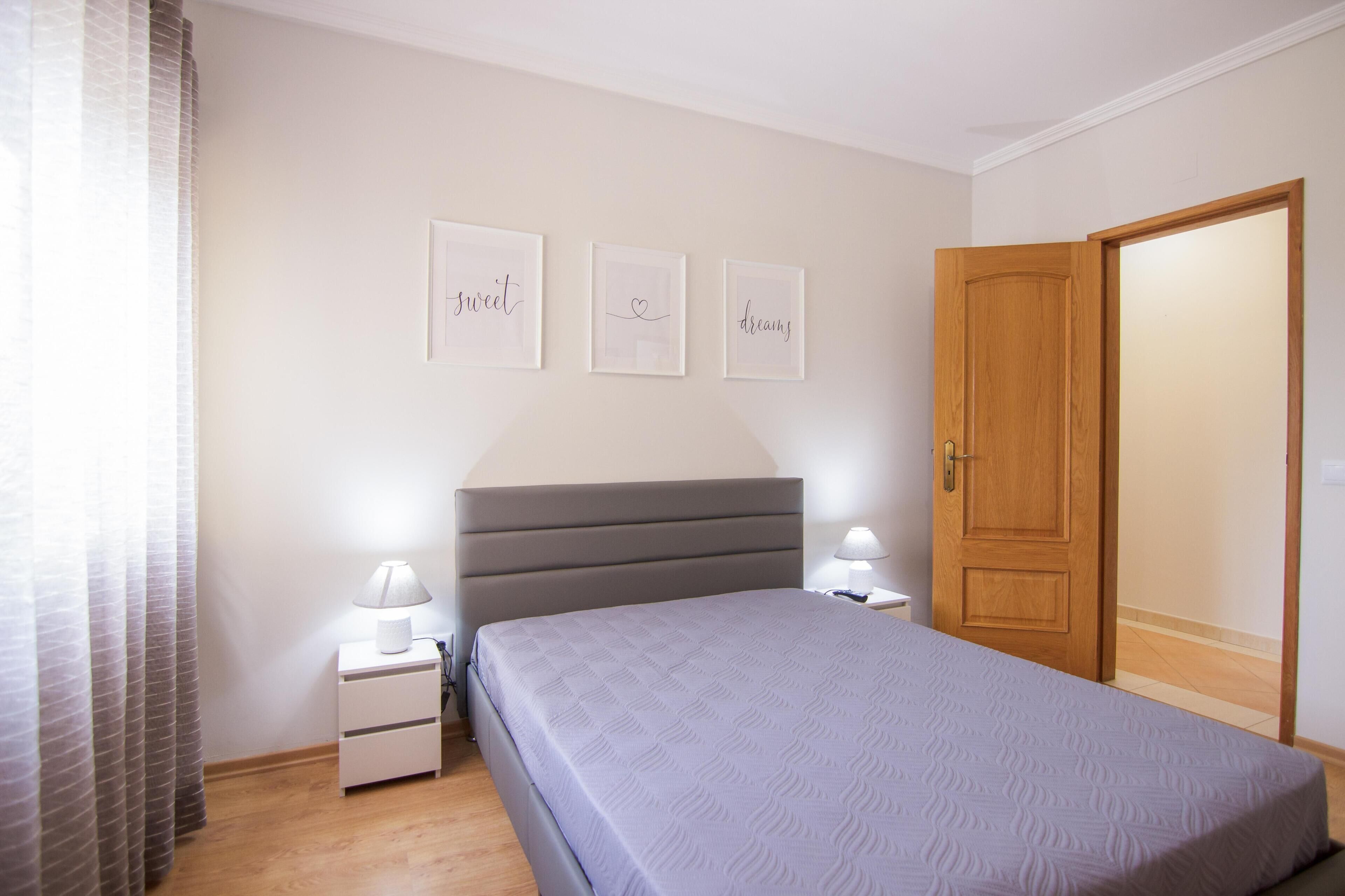 A bedroom with a bed, bedside tables, a nightstand, a wooden door, and three framed pictures on the wall.