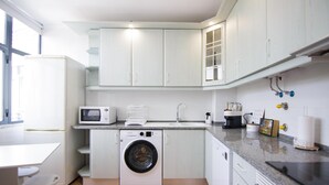 A compact kitchen with a washing machine, microwave, and a coffee maker. - Modern 3-Bedroom Retreat in. Faro’s City Center (Faro)