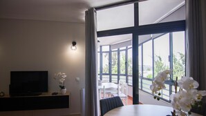 A modern living room with a flat-screen TV, a potted orchid, and a dining area with a table and chairs. - Modern 3-Bedroom Retreat in. Faro’s City Center (Faro)