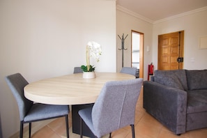 A dining area with a round table, two grey chairs, and a potted orchid.
