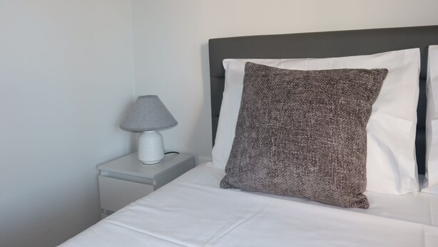 A neatly made bed with white bedding and a gray textured pillow. - Modern 3-Bedroom Retreat in. Faro’s City Center (Faro)