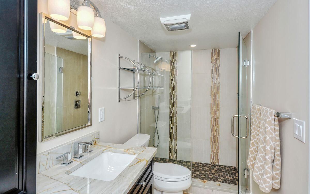A modern bathroom with a glass shower enclosure, a white toilet, and a marble sink.