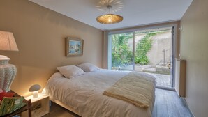 Une chambre à coucher avec un lit, une lampe de chevet, un tableau au mur et une vue sur un jardin, visible à travers une porte coulissante.