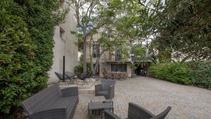Une terrasse extérieure avec des meubles en osier, un sol carrelé et un bâtiment en arrière-plan.