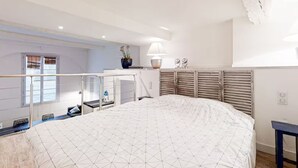 A bedroom with a large bed, a window with blinds, a bedside table with a lamp, and a small plant. - Charm and comfort in the heart of the historic city (Nice)