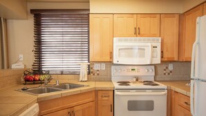 A kitchen with wooden cabinets, a white stove, a microwave, and a double sink. - Kingsbury Of Tahoe (Stateline)