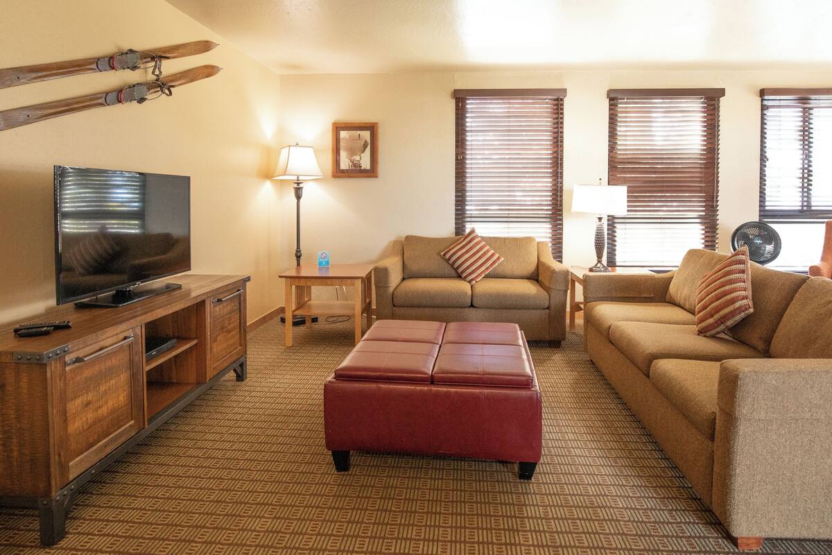 A living room with a television, sofa, ottoman, and a wooden cabinet.