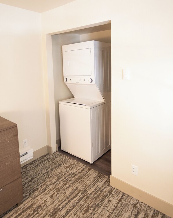 A compact laundry room with a front-loading washer and dryer, carpeted floor, and a wooden cabinet.