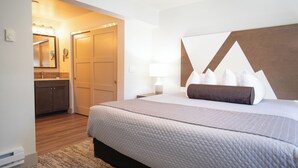 A hotel room with a bed, a nightstand, a lamp, a dresser, and a bathroom visible through an open door. - Tahoe Trail (Stateline)