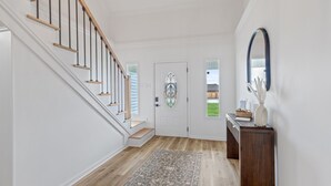 A clean, modern hallway with a wooden staircase, a patterned rug, and a dark wooden console table with decorative items.