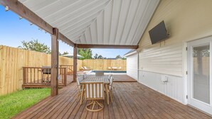 A covered patio with a wooden deck, a pool, and a white exterior wall.