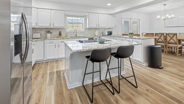 A modern kitchen with white cabinetry, a large island with bar stools, and a dining area with wooden chairs.