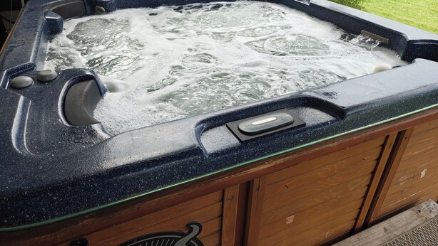 A hot tub with a control panel, a wooden cabinet, and a grassy yard in the background. - Pointer Palace (South Point)