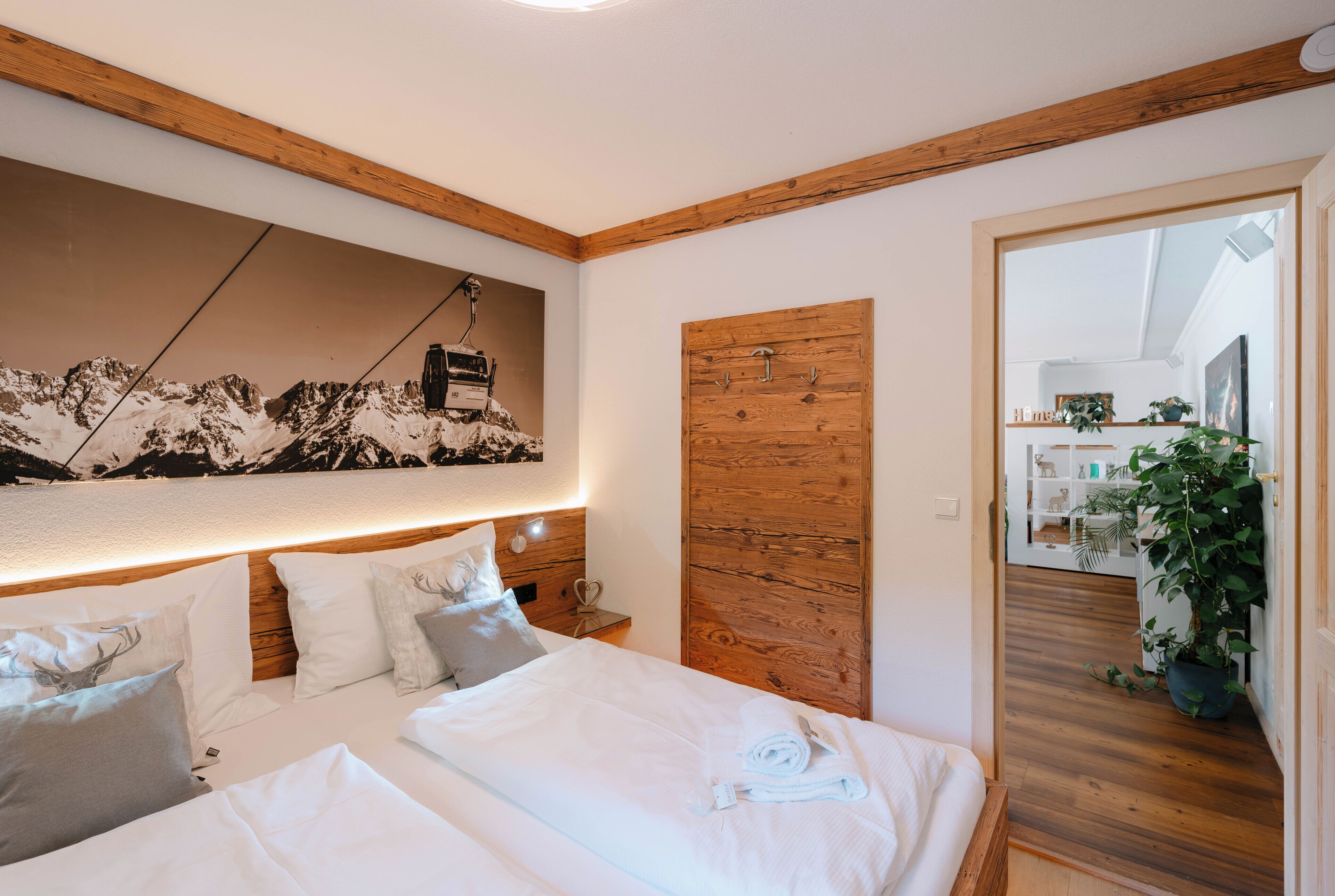 A bedroom with a wooden ceiling, a bed with white linens, a wooden headboard, and a mountain landscape painting.
