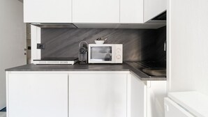Een kleine keuken met witte kastjes, een magnetron en een fornuis.