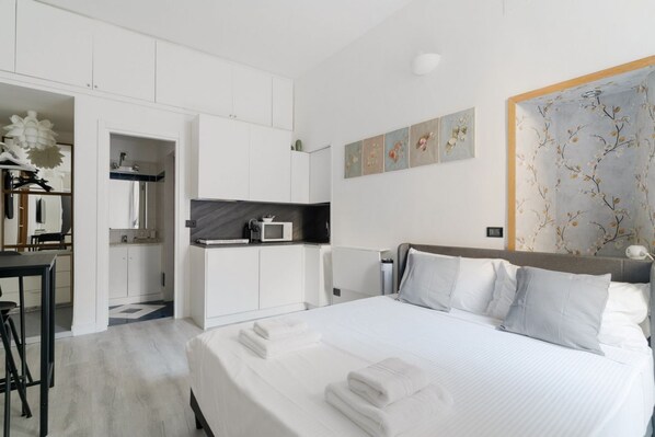 A modern hotel room with a large bed, a separate kitchenette, a dining area, and a bathroom.