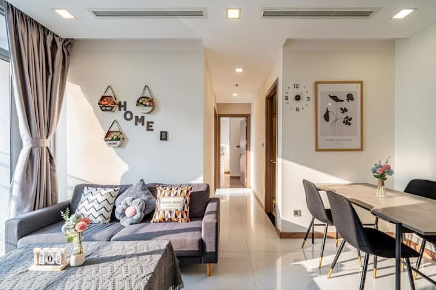 A modern living room with a sofa, a dining table with chairs, and a hallway leading to another room.