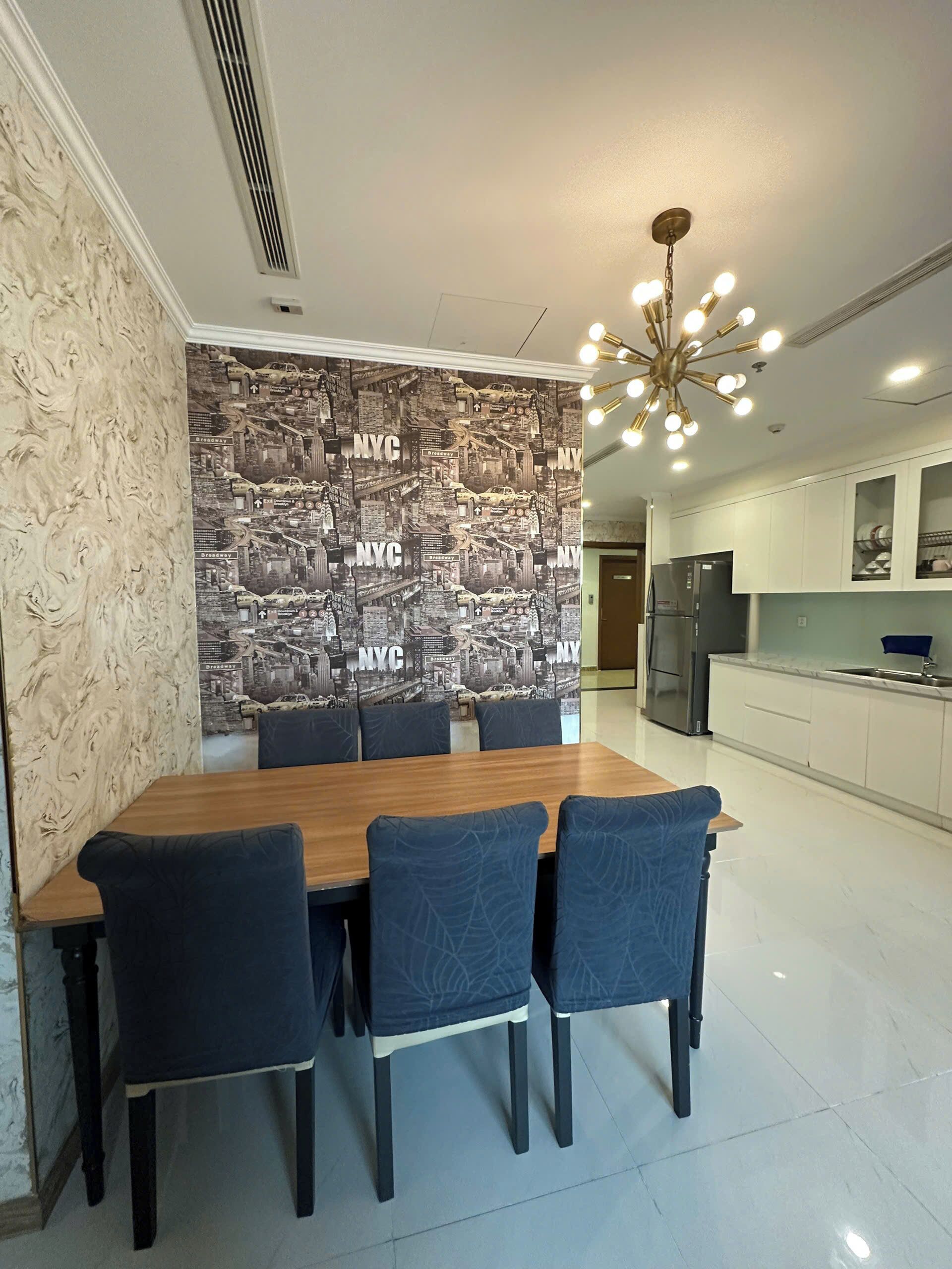 Un comedor con una mesa de madera y cuatro sillas, una pared con un mural de la ciudad, y una cocina moderna al fondo.