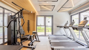 Un gimnasio con equipamiento de ejercicio, cintas de correr y ventanas amplias.
