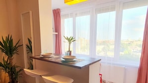 A kitchen with a bar counter, two stools, a potted plant, and a window with a city view. - NEW. Take Panorama Studio Apartment: AC, jalouise (Timișoara)