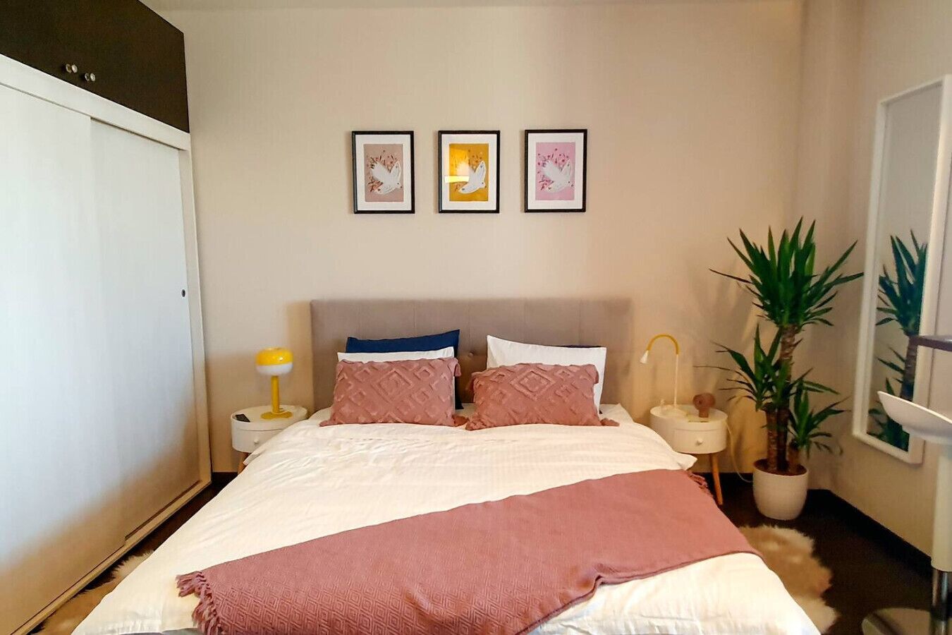 A bedroom with a bed, pillows, a blanket, bedside tables, a lamp, and wall art.