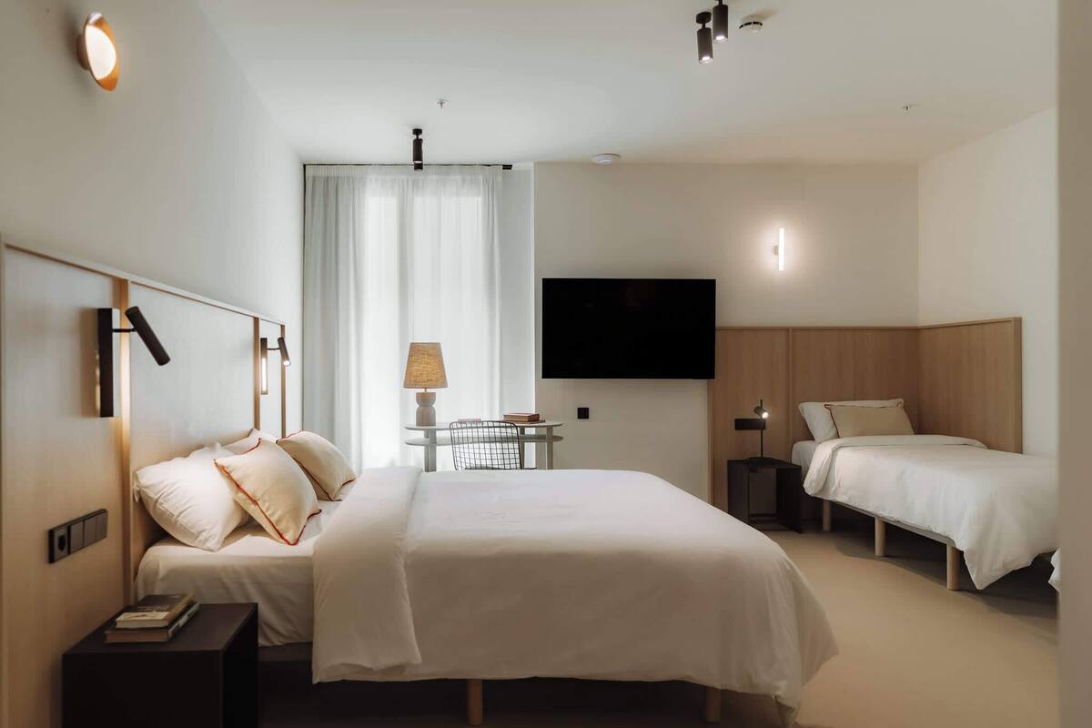 Una habitación de hotel con dos camas, televisión, lámpara y una mesita.