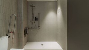 Un área de ducha moderna con puerta de cristal, cabezal de ducha de mano y grifo empotrado.