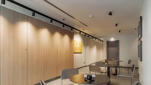 Una sala de conferencias moderna con paneles de madera, mesas redondas y sillas de metal.