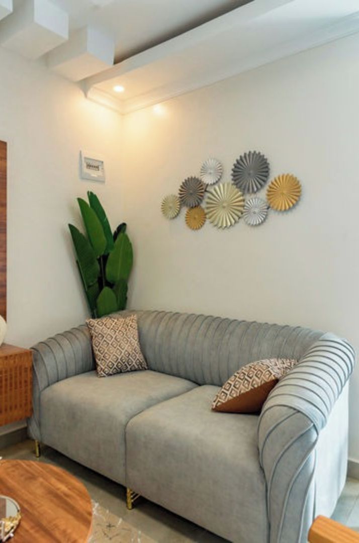 Ein modernes Wohnzimmer mit einem grauen Sofa, gemusterten Kissen, einem Holzbeistelltisch und einem runden Couchtisch. Dekorative Papierbilder sind über dem Sofa an der Wand angebracht.
