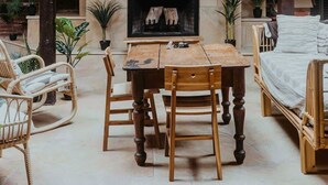 Un espace patio accueillant avec une table et des chaises en bois, une cheminée et un téléviseur fixé au-dessus.