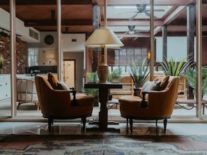 Quarto com duas poltronas de couro, uma mesa com abajur e vista para uma cozinha e sala de jantar através de amplas janelas.